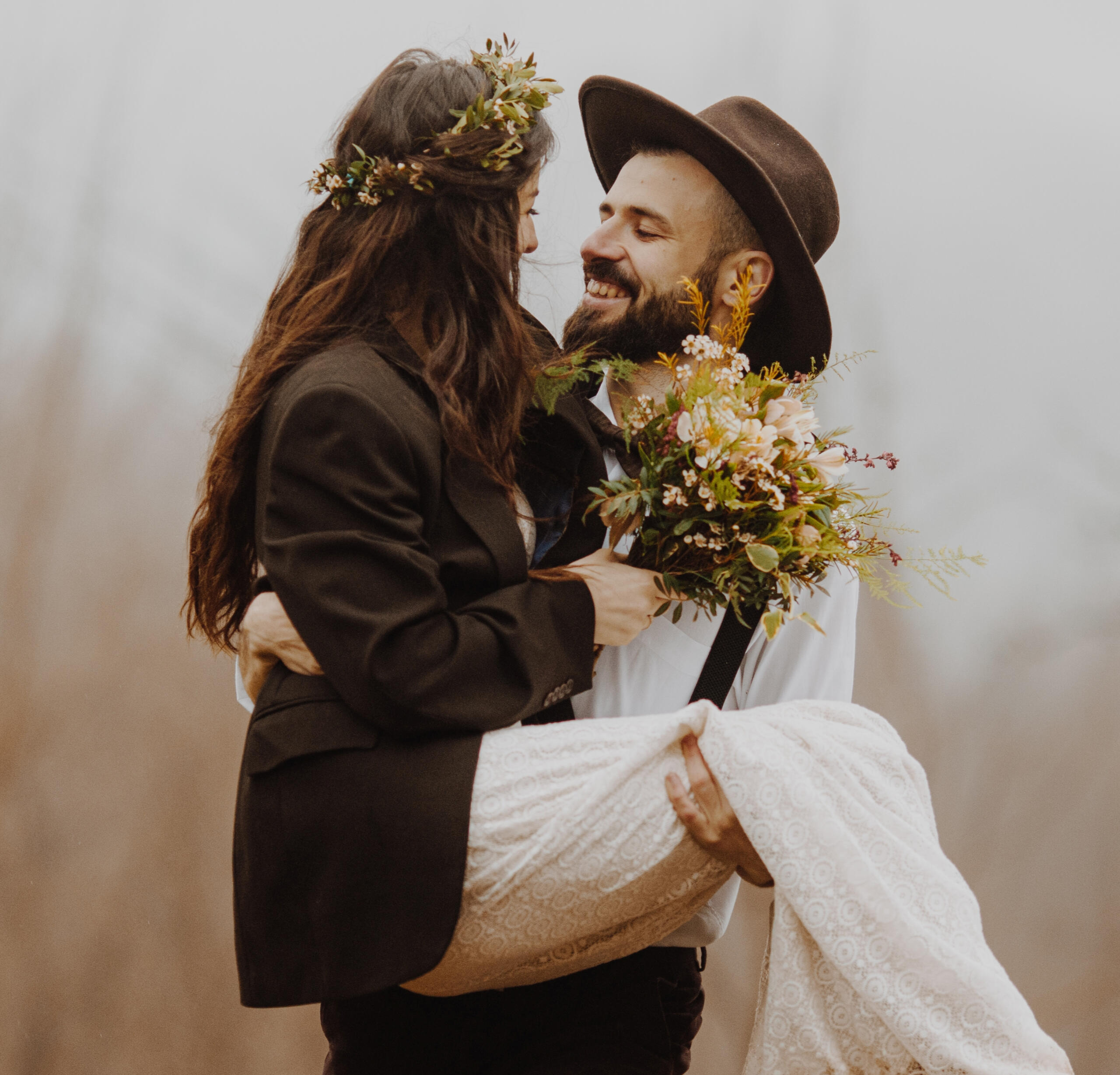 Boho couple, man carrying his new wife at outdoor wedding ceremony